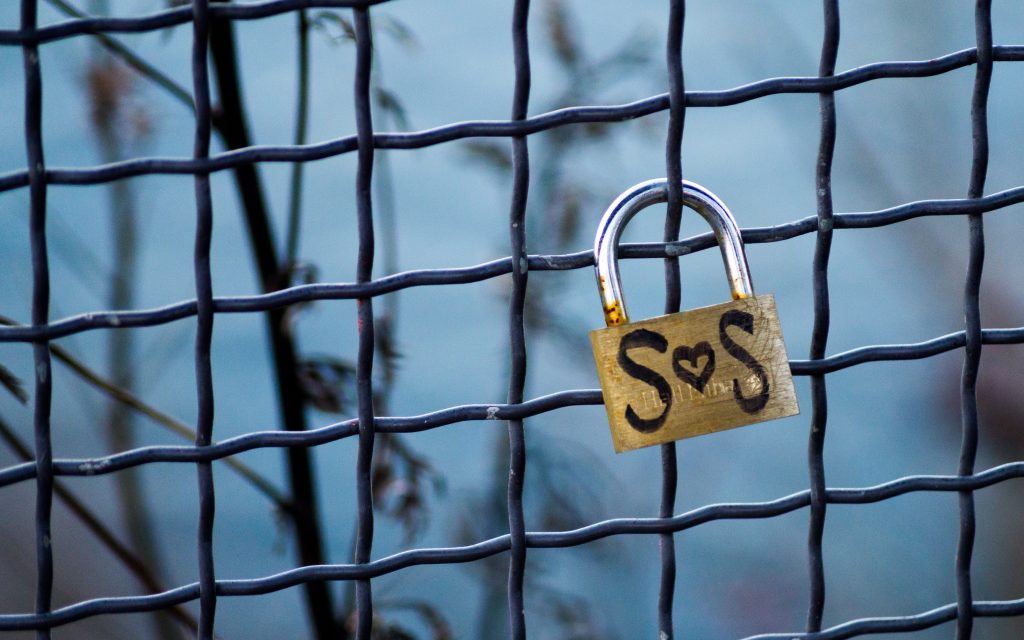 cadenas avec l'inscription SOS  accroché à une grille métallique 