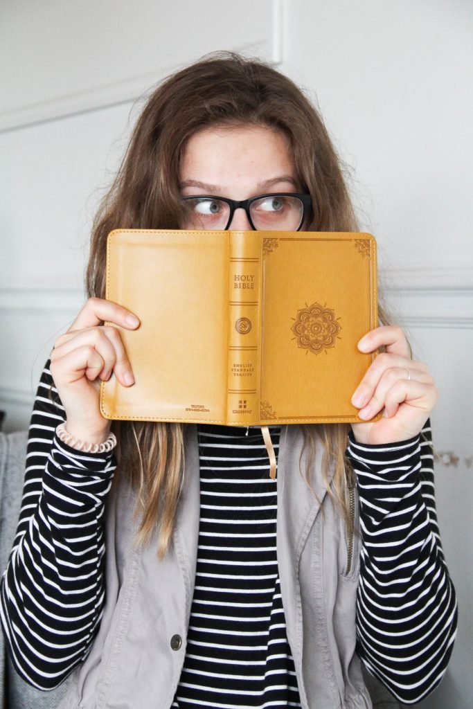 Une jeune fille tient une Bible ouverte devant son visage. On ne voit que le haut de son visage et ses yeux, qui trahissent un grand étonnement.