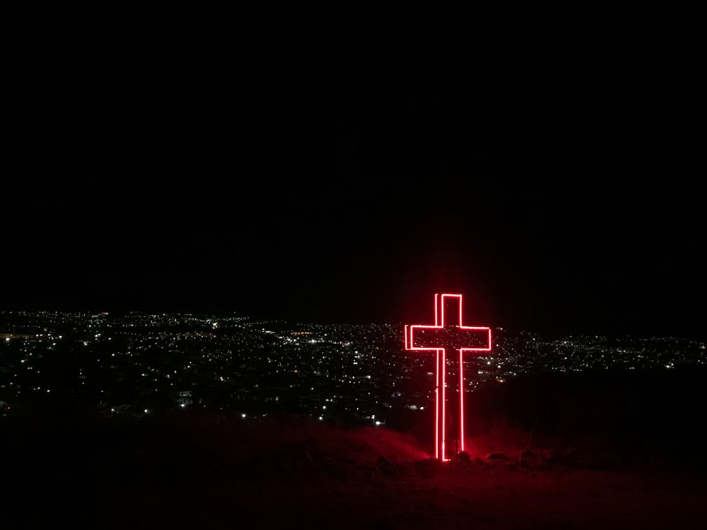 une grande croix est allumée dans la nuit avec les lumières d'une ville en arrière-fond