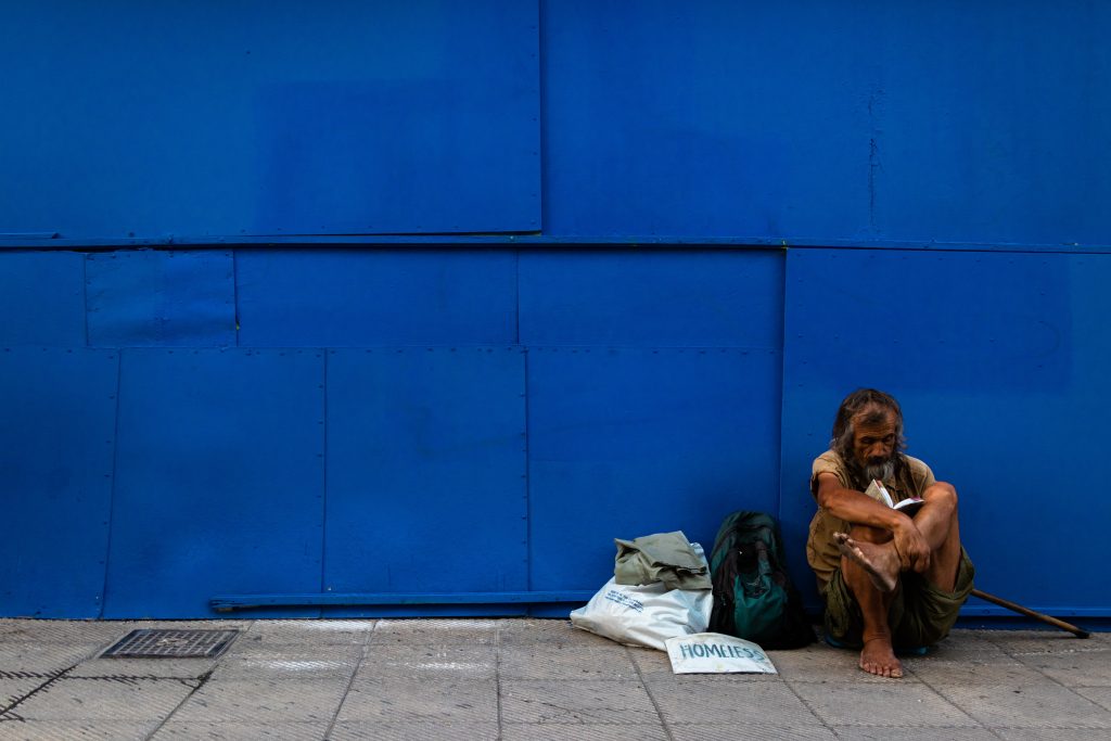 un homme seul, visiblement pauvre comme Job, sans abri, assis sur le trottoir, au bord d'un bâtiment