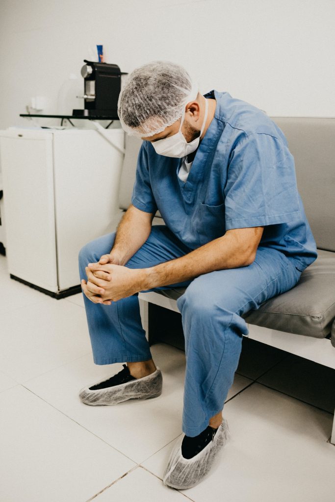 Faire tomber les masques, vraiment ? 
Un infirmier à l'hôpital, à la cafétéria, portant masque et charlotte, assis et en train de prier 