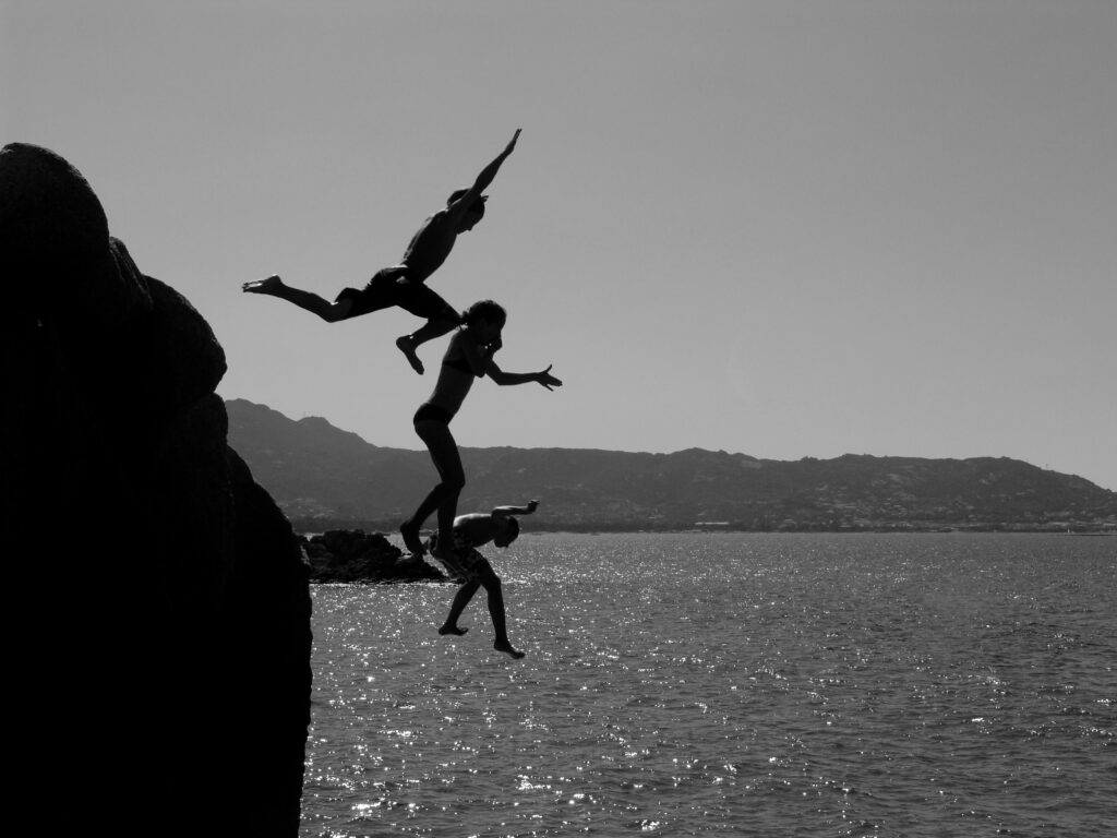 Trois personnes sautant, du haut d'une grande falaise, dans la mer 