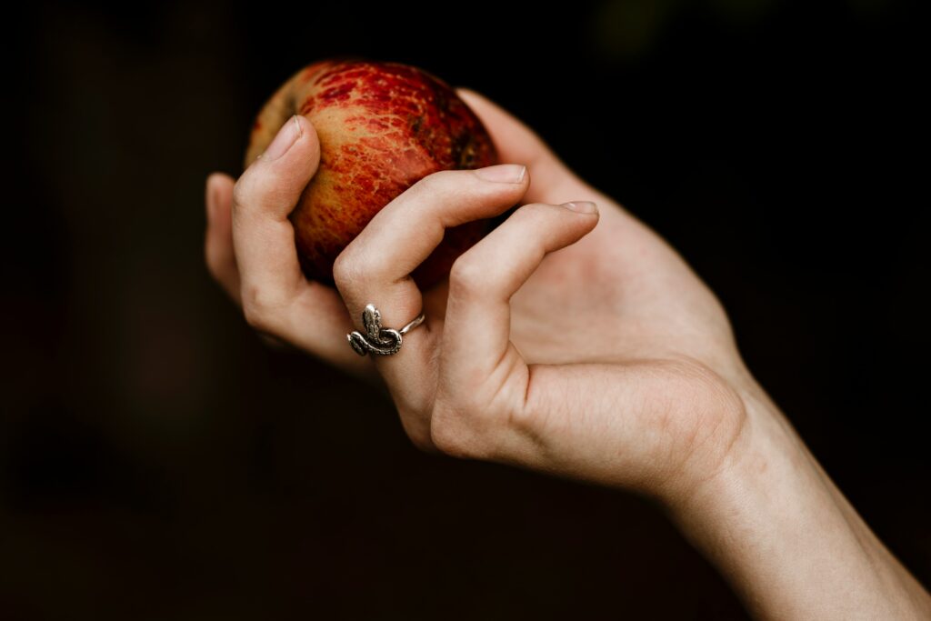 Une main tendant une pomme, le tout sur fond noir, belle illustration symbolique de notre cours sur les repas dans la Bible