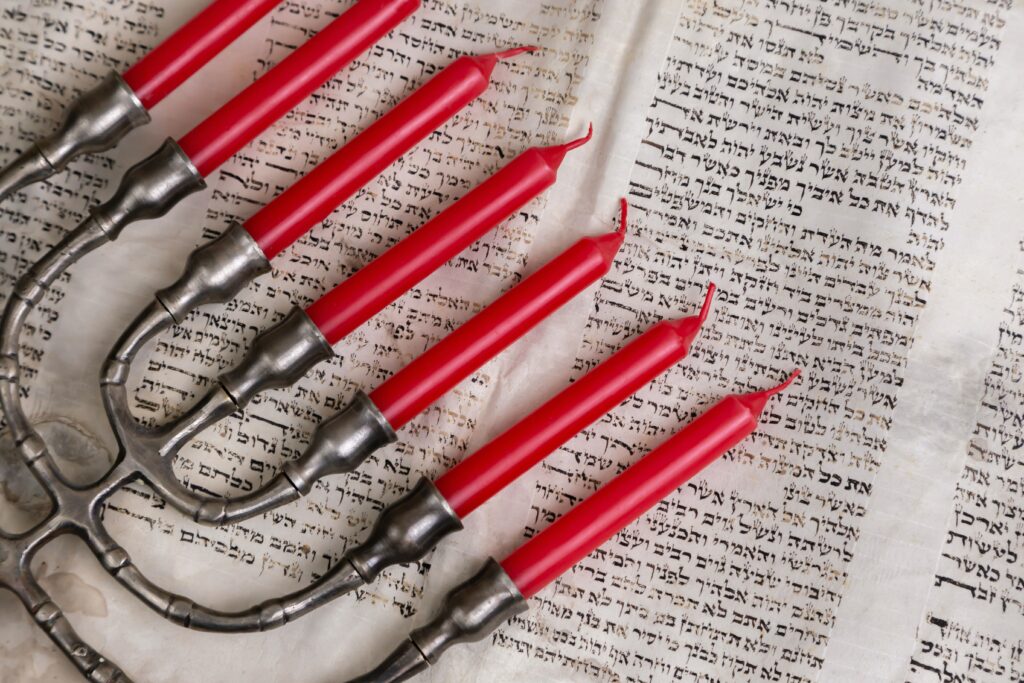 Un chandelier à sept branches, avec des bougies rouges, posé sur une bible en langue hébraïque, pour illustrer notre présentation de l'introduction à l'Ancien Testament