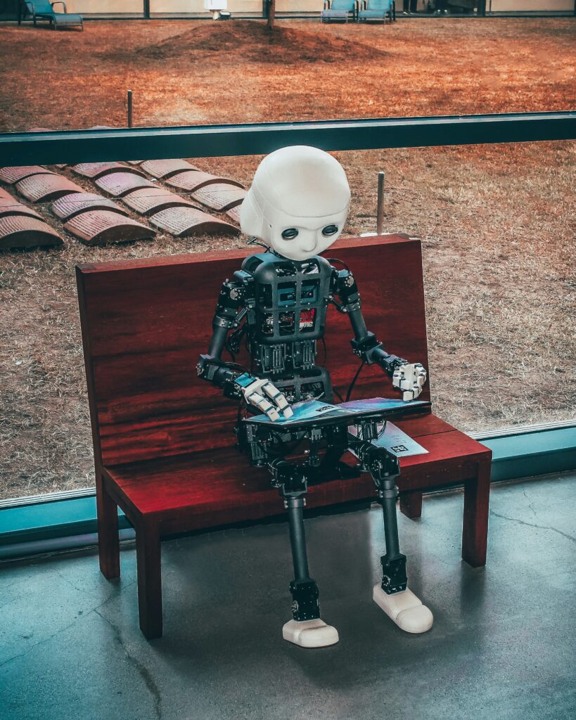 Pourquoi lire les livres des Rois avec Chat GPT? Sur la photo, un robot assis sur un banc public en train de feuilleter un document sur ses genoux